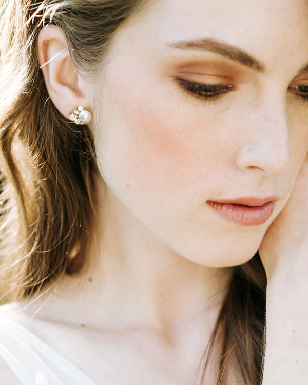 A close-up on a model wearing the Celestial Pearl Cluster Earrings in gold with cream faux pearls. She is wearing them with the crystals to the side, instead of to the bottom.