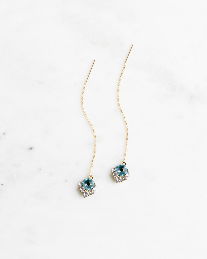 Flatlay of the Celestial Crystal Threader Earrings in gold with aquamarine crystals.