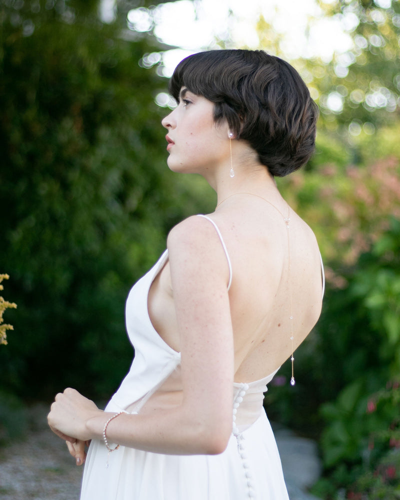 A bride models the Crystal Back Drape in gold alongside the Dewdrop Luxe Long Earrings.