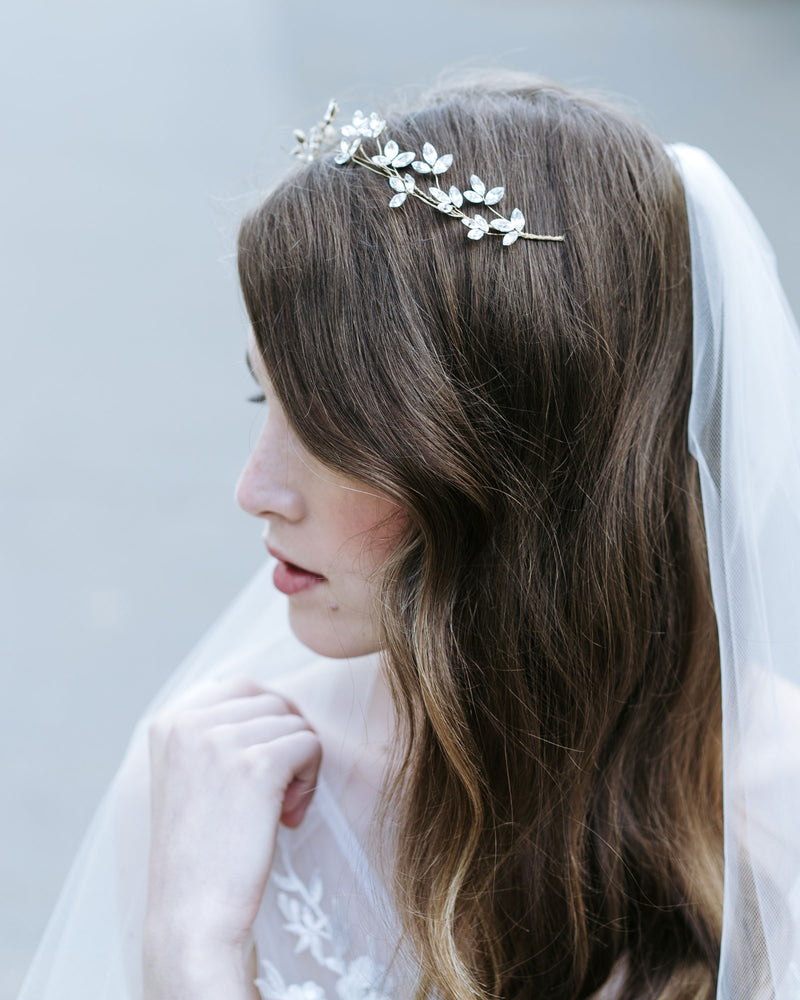 A bride poses wearing a delicate crystal blossom hair vine in soft bridal waves. She is also wearing a soft tulle veil.