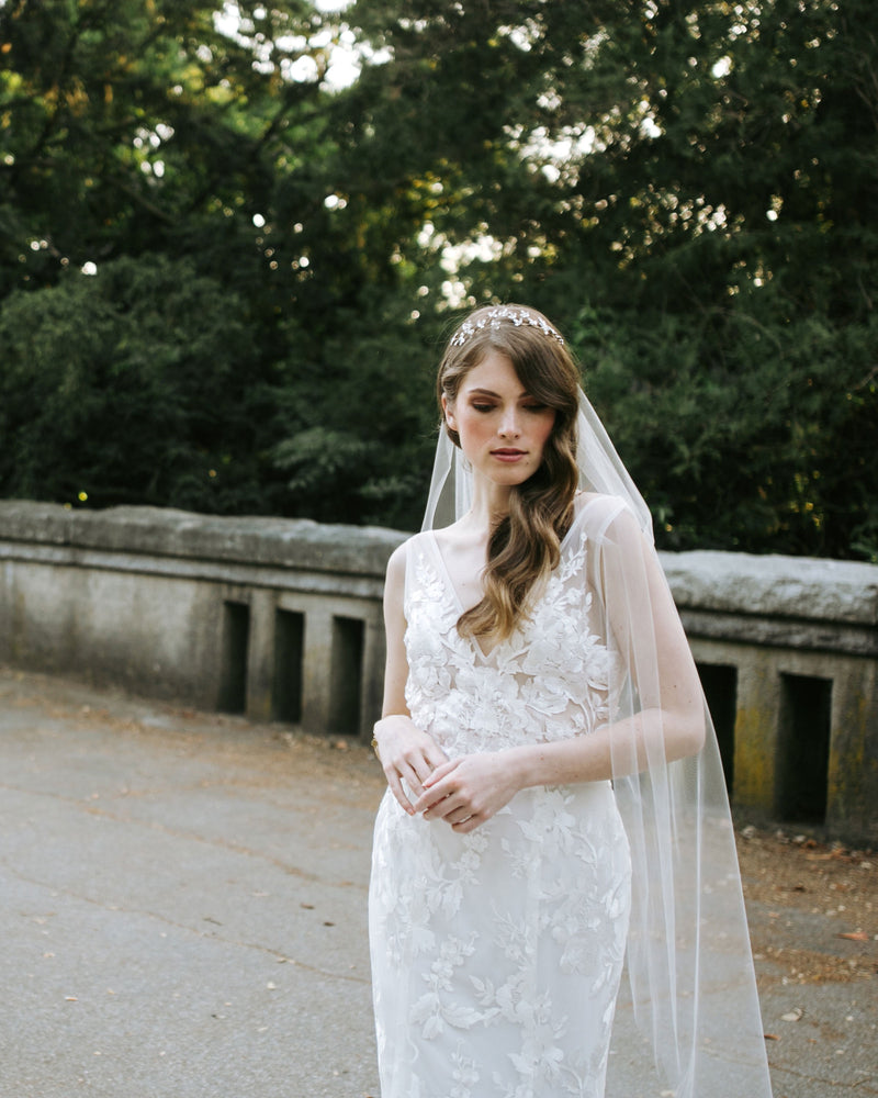 A model poses at Stanley Park, wearing a crystal blossom hair vine in soft bridal waves. She is also wearing a soft tulle veil.