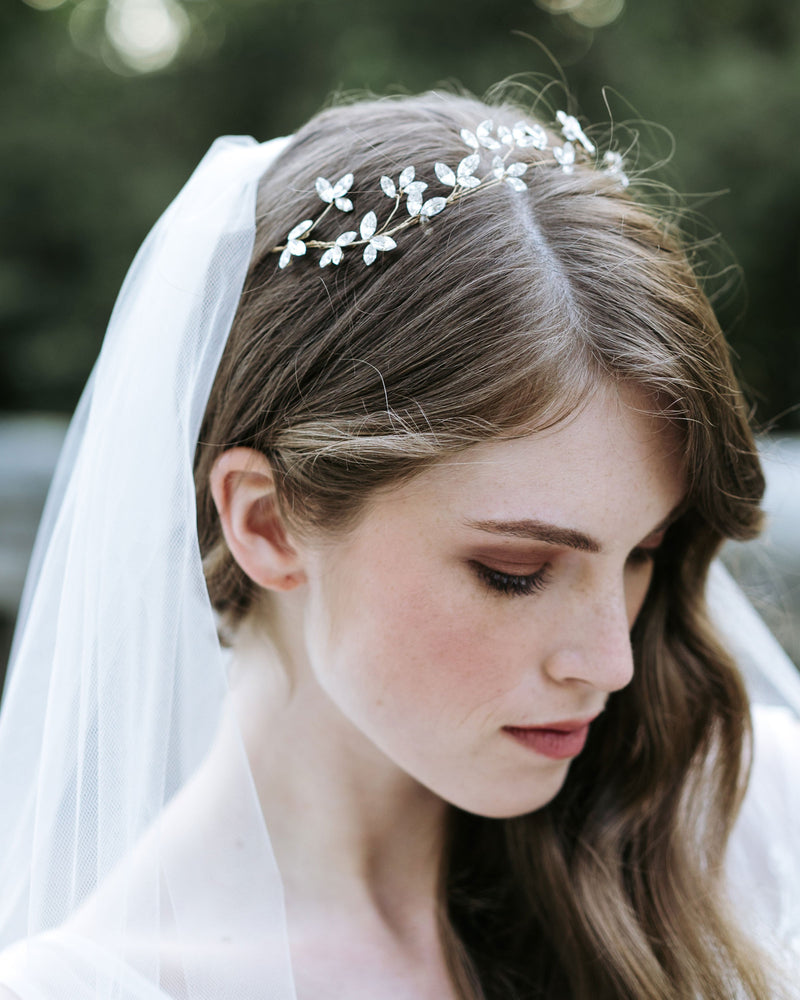 A bride poses wearing a delicate crystal blossom hair vine in soft bridal waves. She is also wearing a soft tulle veil.
