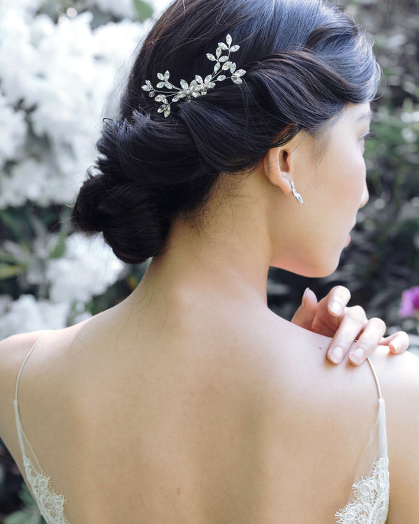A dark-haired bride with a low bridal updo is wearing a crystal bridal comb made of crystal leaf clusters.