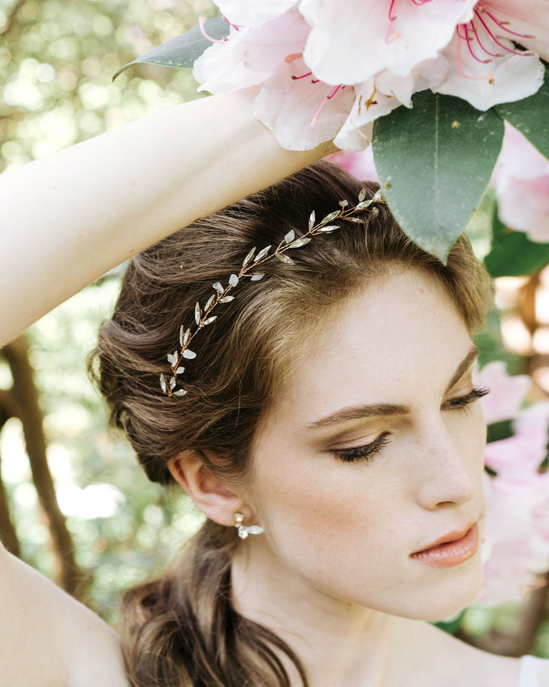 A bride wears our crystal leaf earrings in gold with a crystal and gemstone leaf hair vine
