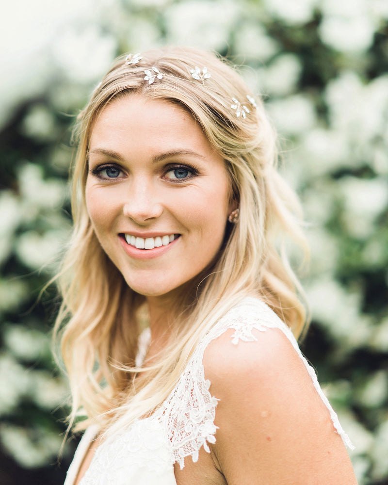 A blonde model smiles into the camera, wearing the Crystal Blossoms Hair Vine in her bridal hairstyle of soft waves, with pieces pinned back.