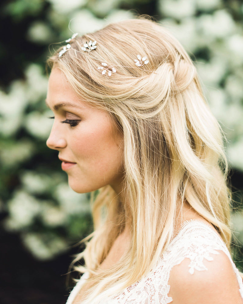 A blonde model wears a delicate hair vine in rose gold made of crystal leaf clusters.