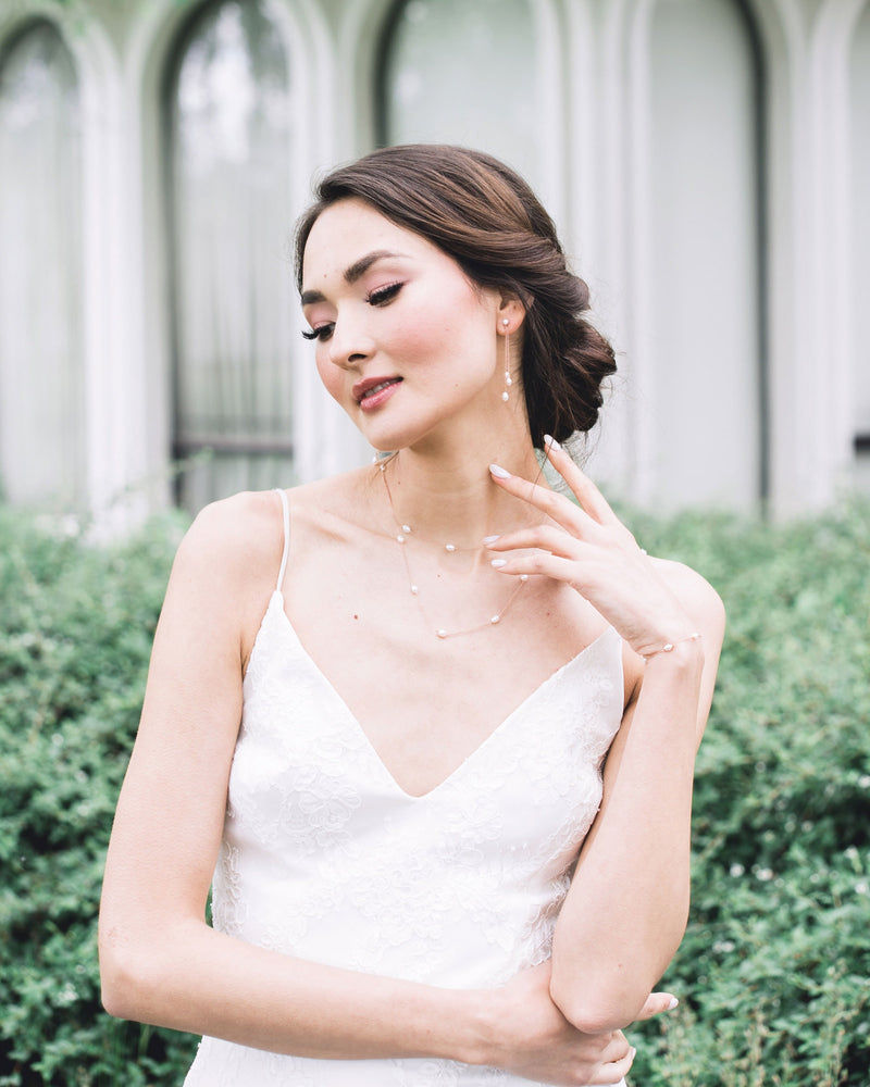 A bride poses in a bridal jewellery set in rose gold. She wears a layered pearl necklace with matching dainty pearl bracelet and long earrings with a trio of pearls.