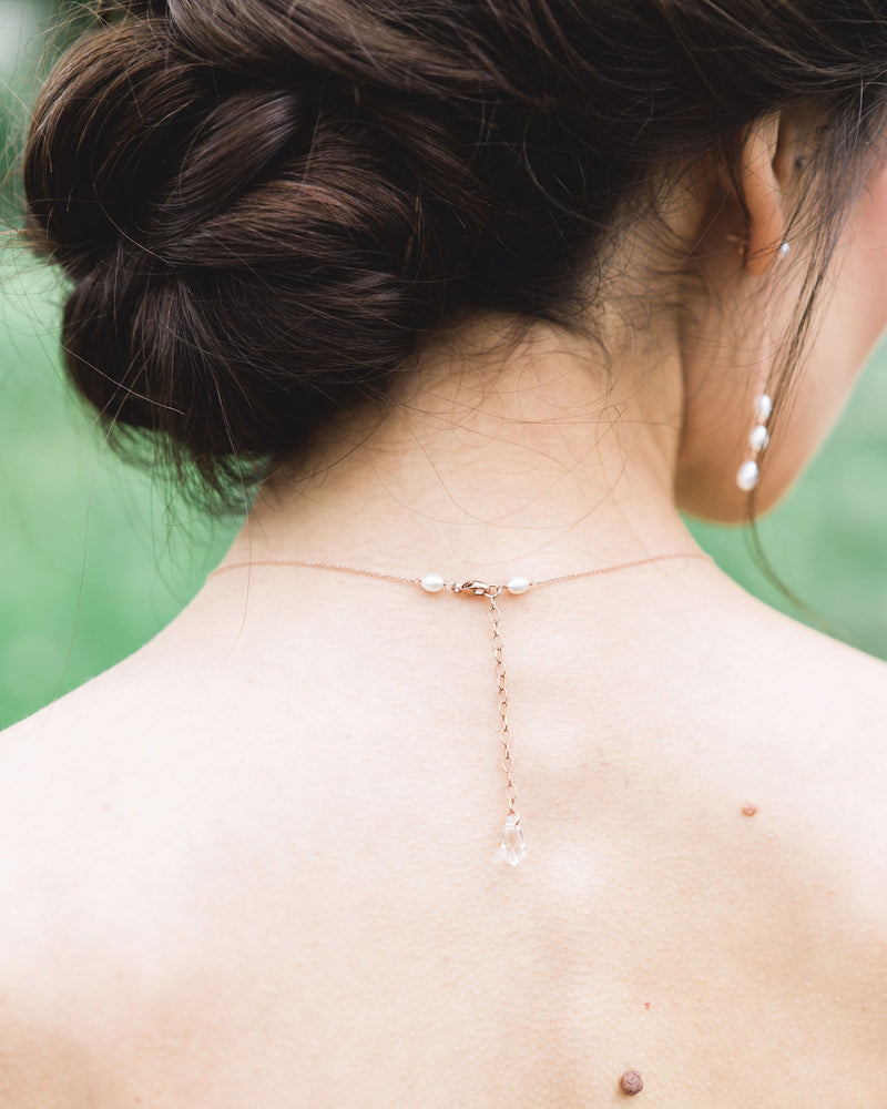 A back view of a model wearing our dainty pearl layered necklace, showing a crystal drop and clasp.