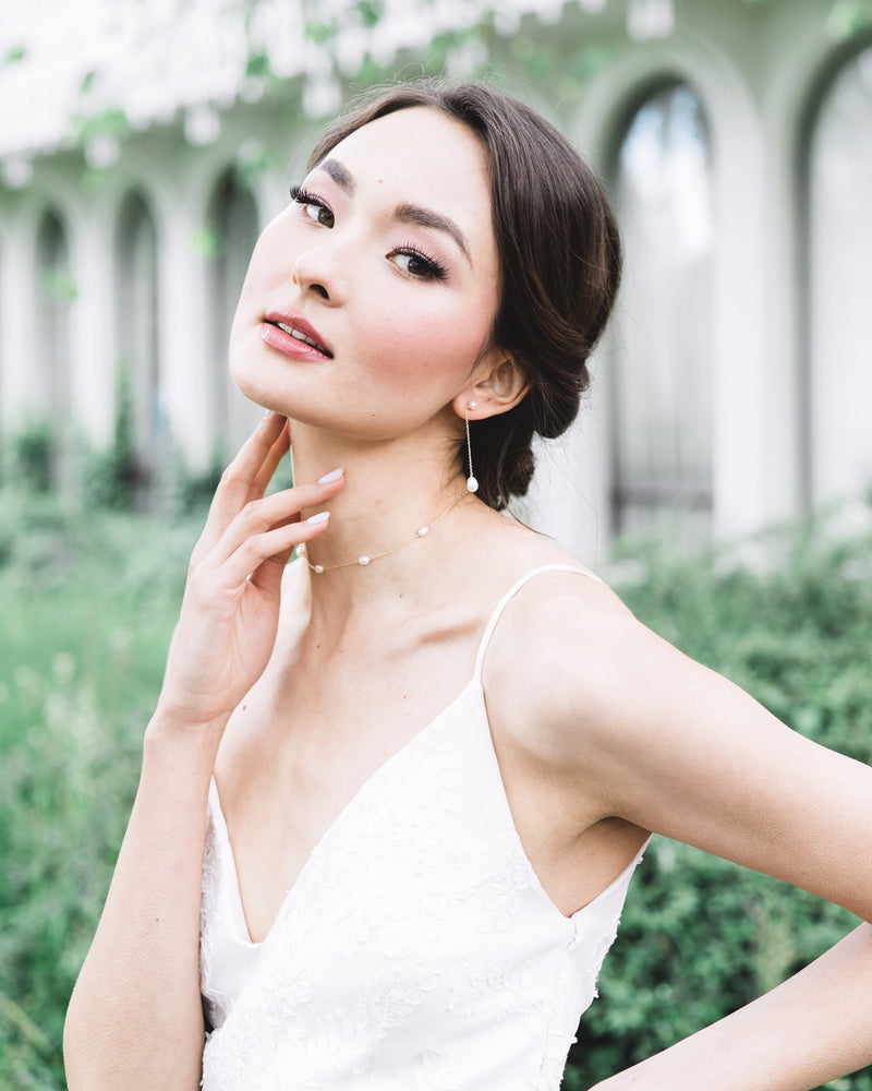A bride with a low bridal updo wears the Dainty Pearl Necklace in gold, paired with the Teardrop Pearl Long Earrings in 2" length.