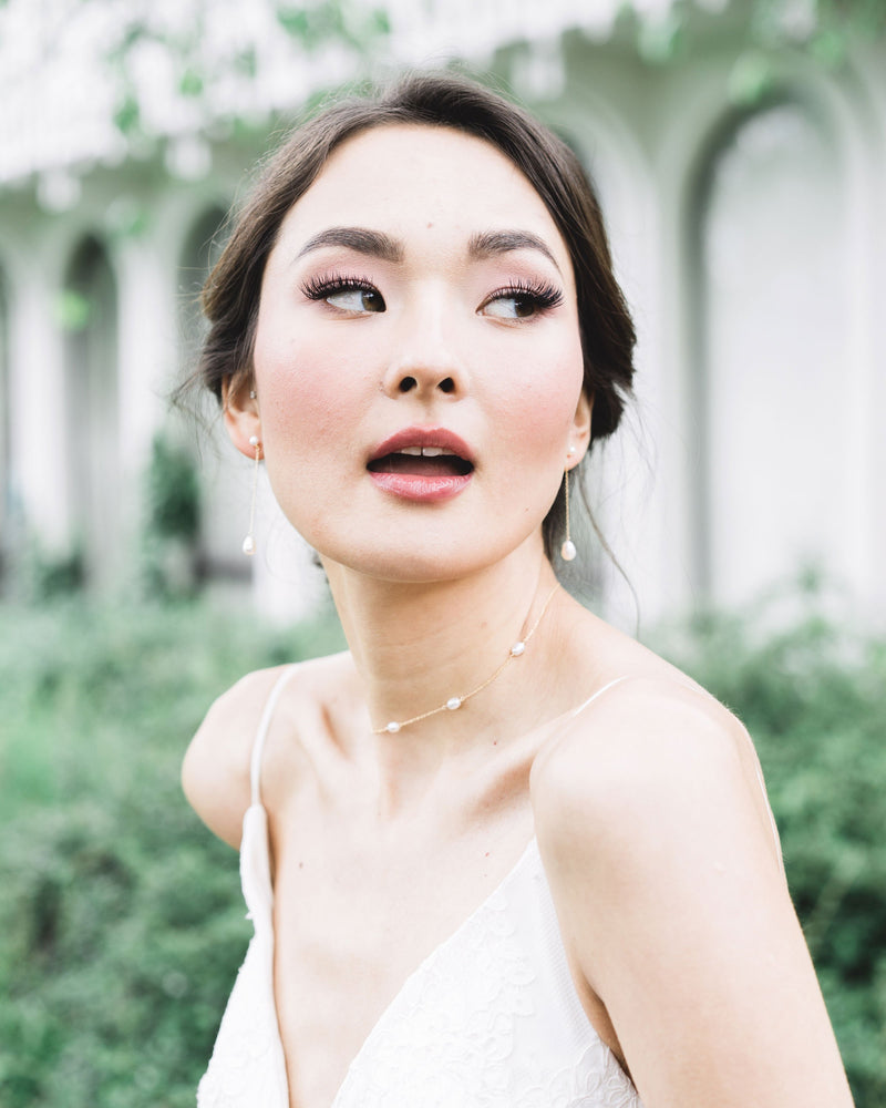A bridal model wears the Dainty Pearl Necklace in gold, paired with the Teardrop Pearl Long Earrings.