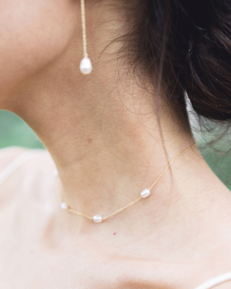 Close-up of the Dainty Pearl Necklace in gold on a model, paired with the Teardrop Pearl Long Earrings.