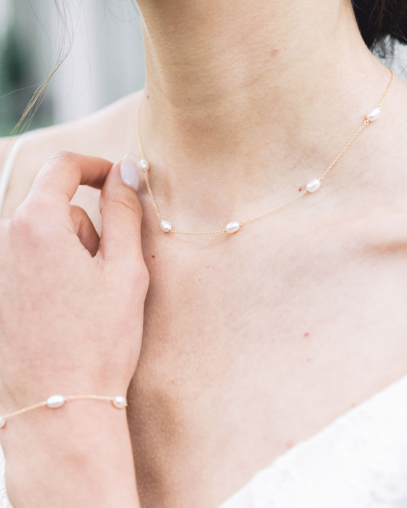 Close-up of the Dainty Pearl Necklace in gold on a model, paired with the Dainty Pearl Bracelet.