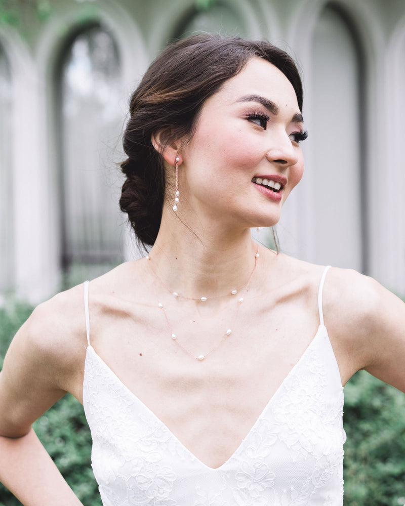 A model wears rose gold bridal jewellery; dainty pearl drop earrings, with a matching layered pearl necklace.