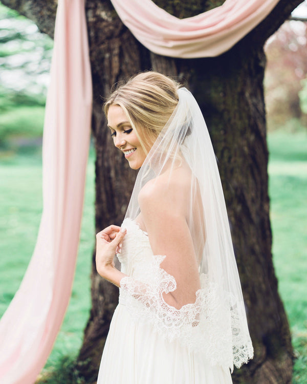A bride is wearing a playful waist veil with an intricate Chantilly lace edge.