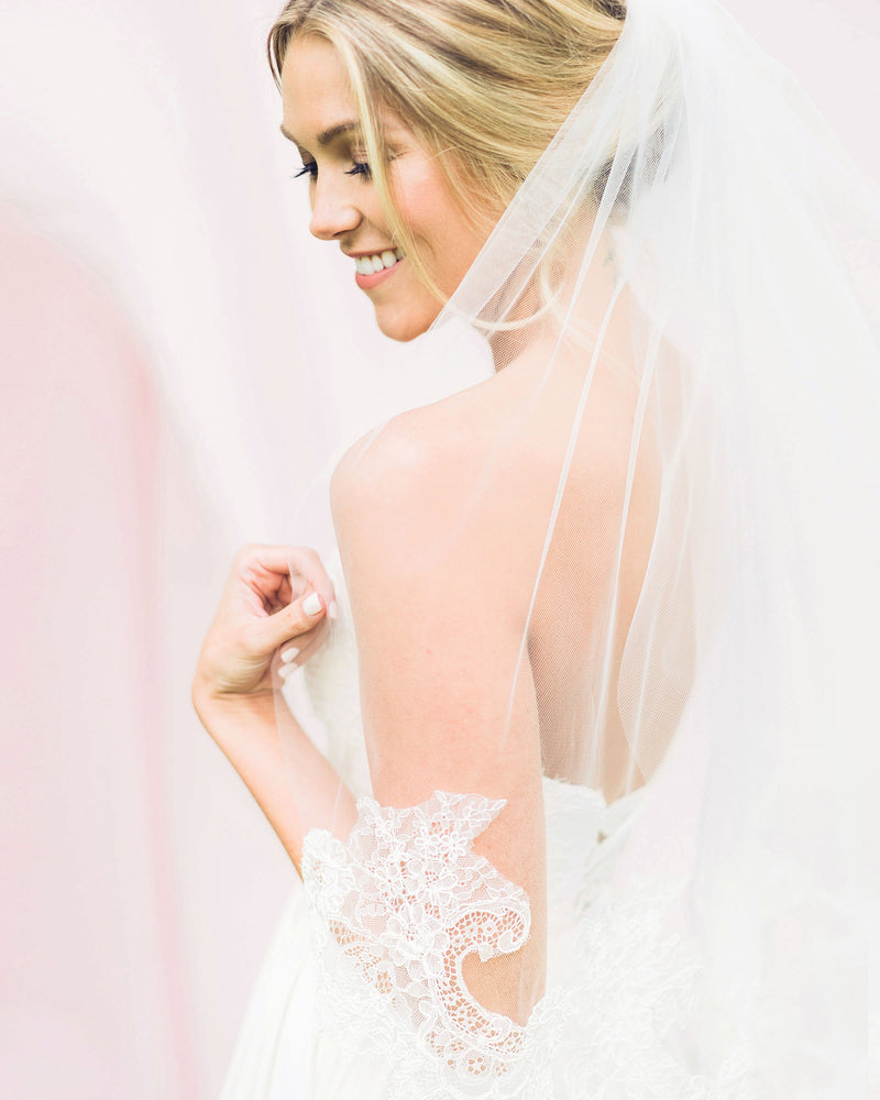 A bride is wearing a playful waist veil with an intricate Chantilly lace edge.