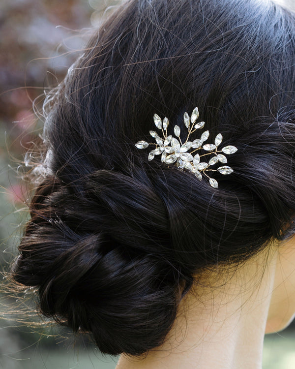 A close model view of the Delicate Comb in gold with only crystals, styled into a low bridal updo with twists and a low bun.