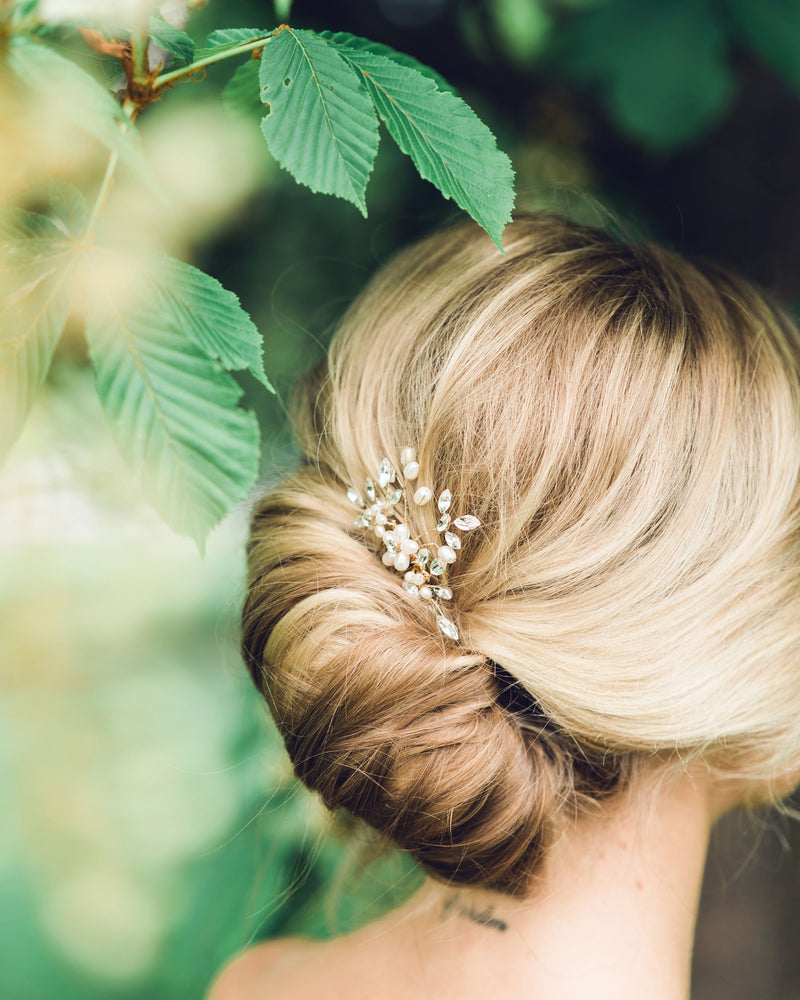 Close model view of the Delicate Comb styled into a modern bridal French twist. The comb is gold with pearls and crystals.