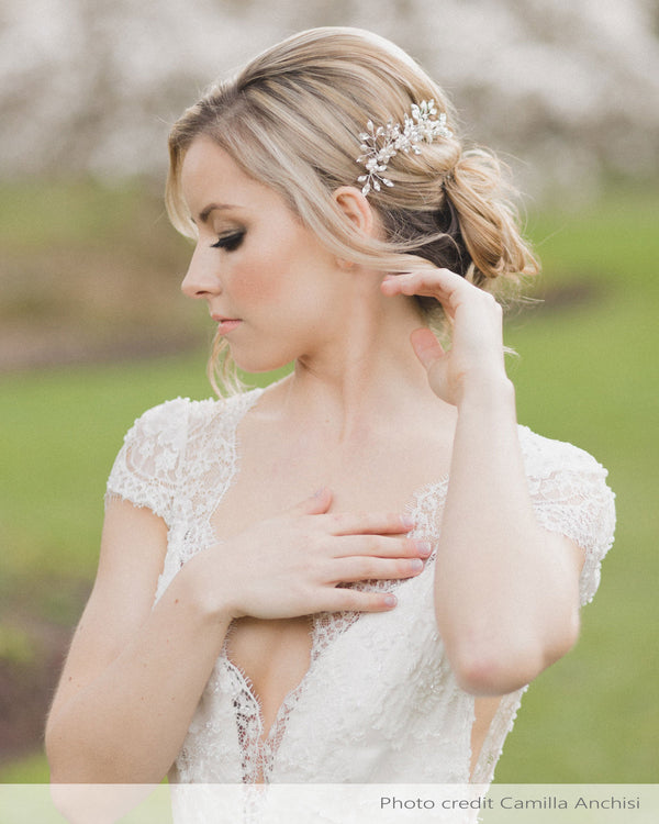 A bride wears a set of two delicate combs with freshwater pearl flowers and crystals styled into her low updo.