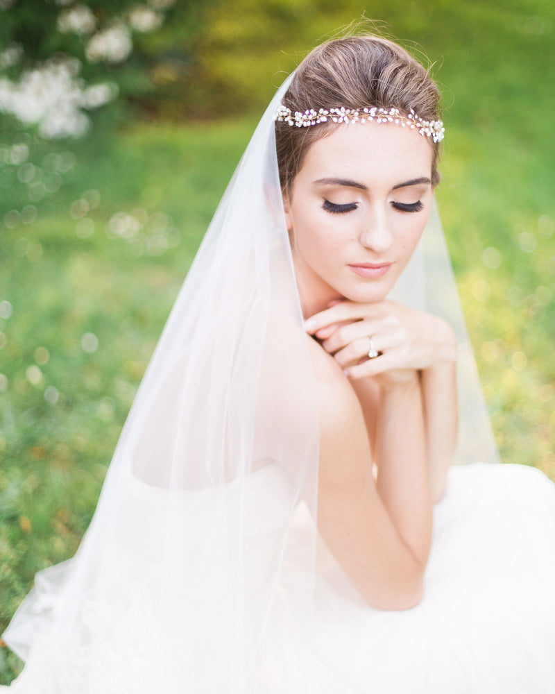 A bride wears a boho headpiece of pearls and crystals with her bridal updo. A soft veil with the blusher to the front covers her face.