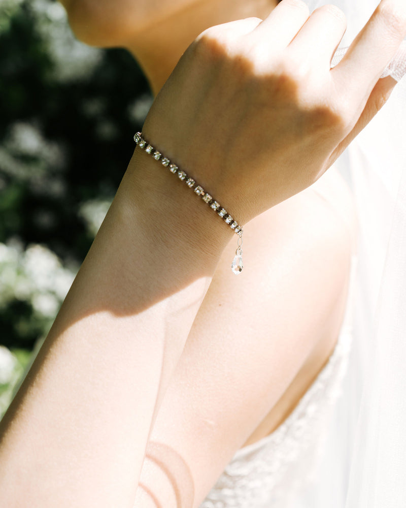 A close model view of the Delicate Tennis Bracelet in silver. The tiny crystal drop on the edge of the extender hangs softly from her wrist.