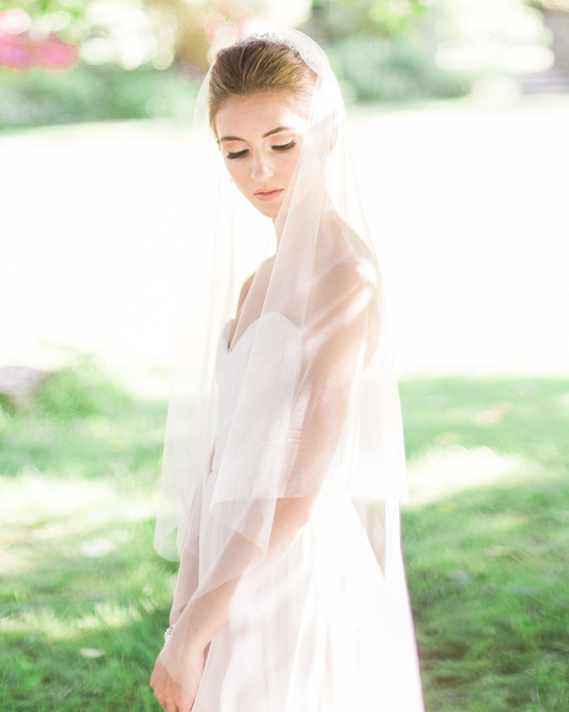 A model poses in a sunlit field. Her two-layer fingertip veil is worn to the back over her bridal updo.