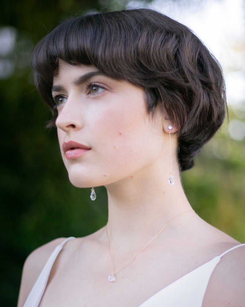 A model wears the Dewdrop Luxe Long Earrings in gold alongside the Dewdrop Crystal Necklace.