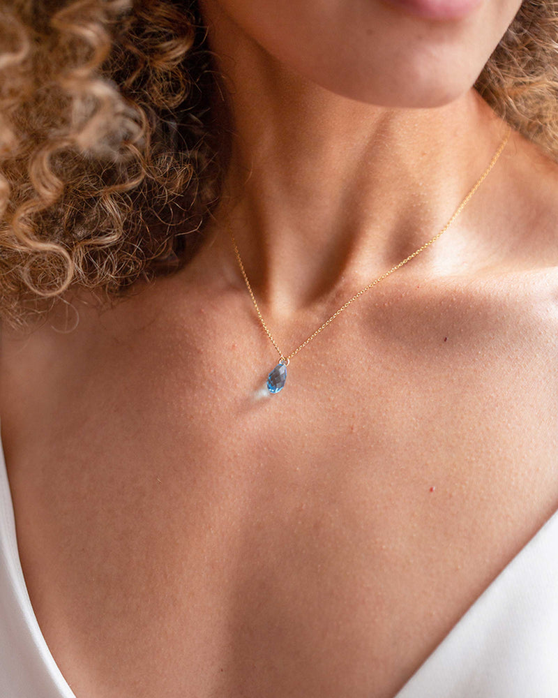 Close model view of the Dewdrop Crystal Necklace in gold with aquamarine crystal.