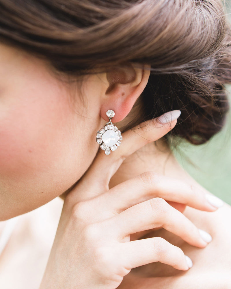 A close model view of a bride wearing the Enchanted Crystal Drop Earrings in silver with white opal centres.