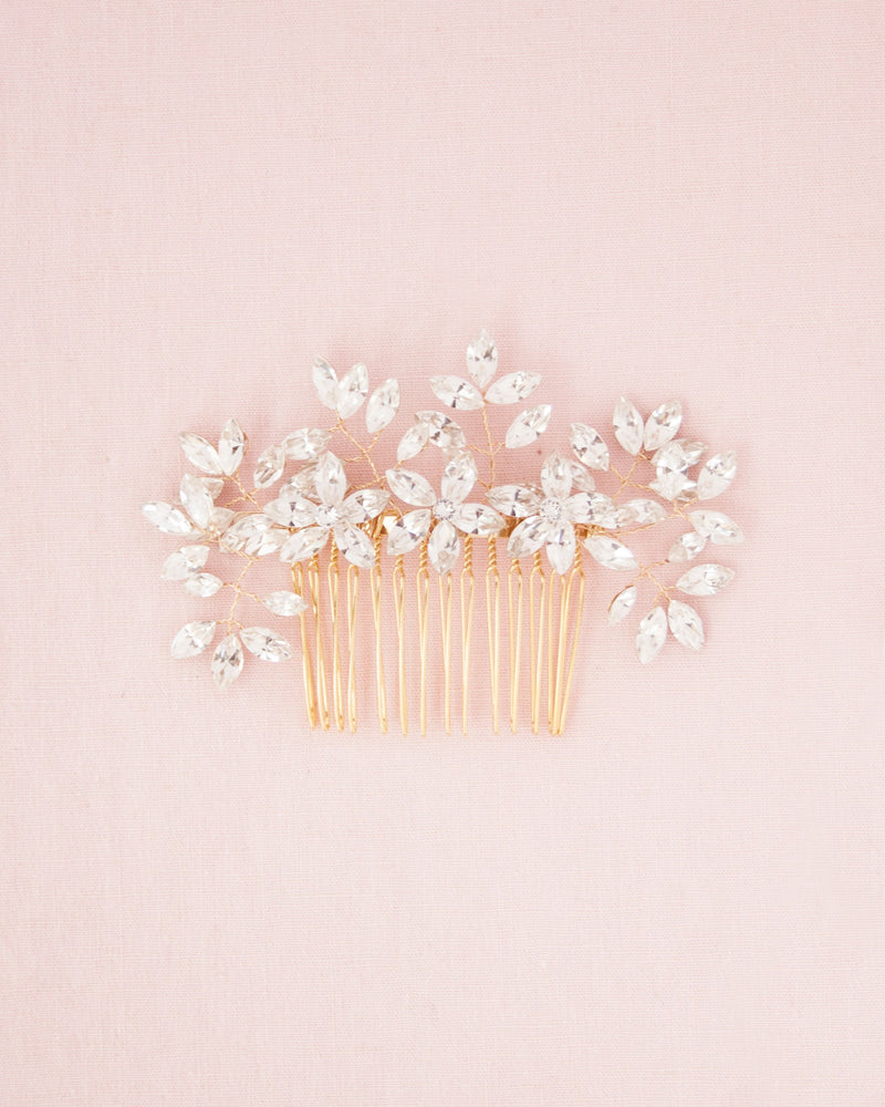 Swarovski crystal bridal comb with delicate sprigs of leaves and flowersA flatlay on a pink background of the Enchanted Crystal Comb in gold.