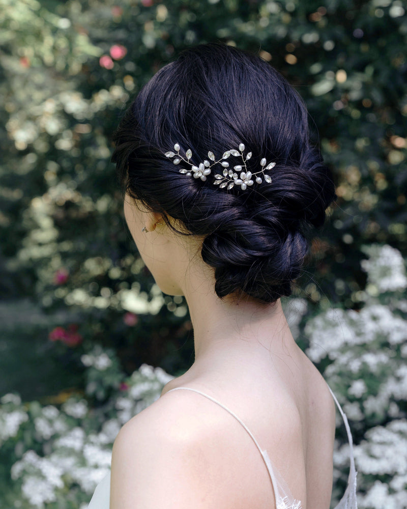 A model has her dark hair styled into a low bridal updo with twists and a braided knot. The Everthine Pearl & Crystal Hair Pins are styled into the back of her updo, slightly to the side.