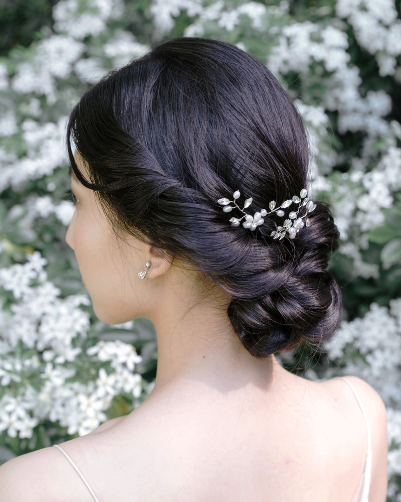 A  dark-haired model has her styled into a low bridal updo with twists and a braided knot. The Everthine Pearl & Crystal Hair Pins are styled into the back of her updo, slightly to the side.