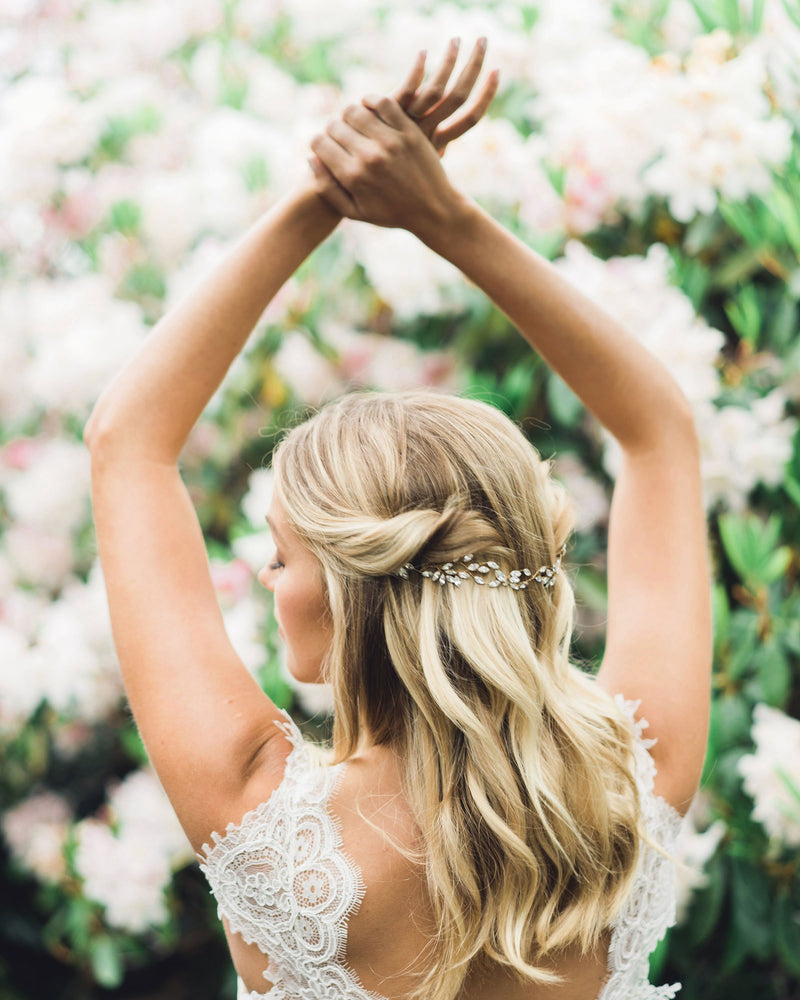 A model stands with her arms gracefully in the air. Her hair is styled in soft waves with the sides pinned back. The Everthine Crystal Hair Vine is styled across the back of her hair.