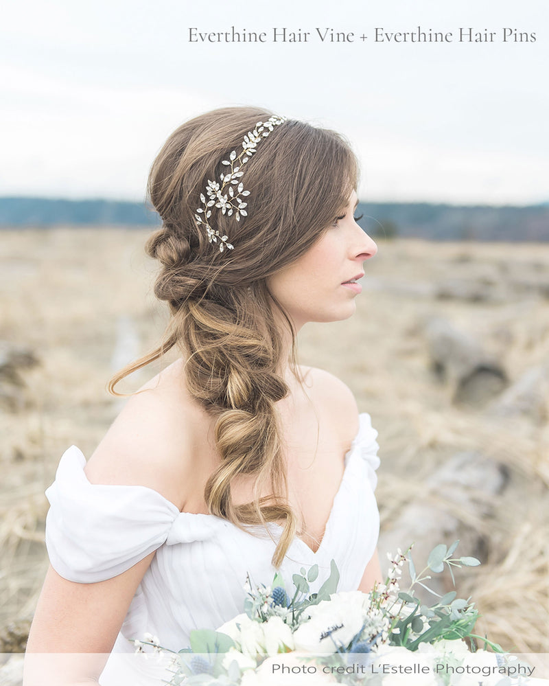 A bride poses at the beach. Her hair is styled down and to the side. She wears the Everthine Crystal Hair Vine, with the Everthine Crystal Hair Pins styled with it.