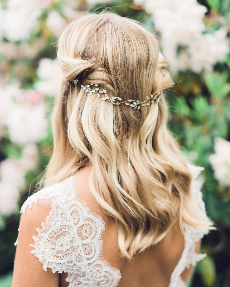 A back view of a model with her hair styled with soft bridal waves and her the sides pinned back. The Everthine Crystal Hair Vine is styled to the back.