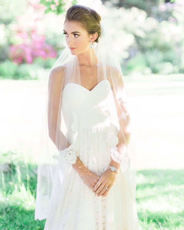 A bride is wearing an illusion tulle lace briModel wearing an airy tulle lace bridal veil with wide Alencon lace scallop.