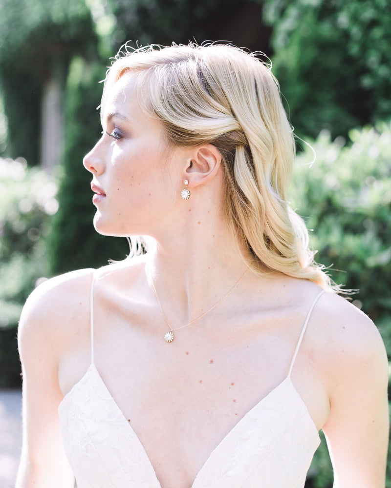 A blonde model with her hair styled in with soft bridal waves is wearing the Halo Pearl Drop Earrings in gold with natural freshwater pearls.