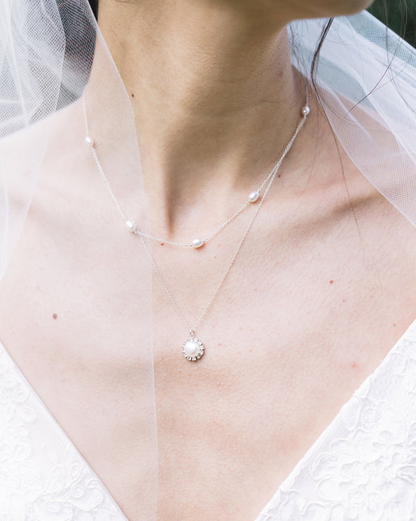 A close on model view of the Halo Pearl Layered Necklace in silver. A freshwater pearl is surrounded by a halo of crystals and hangs beneath a second layer of scattered pearls.