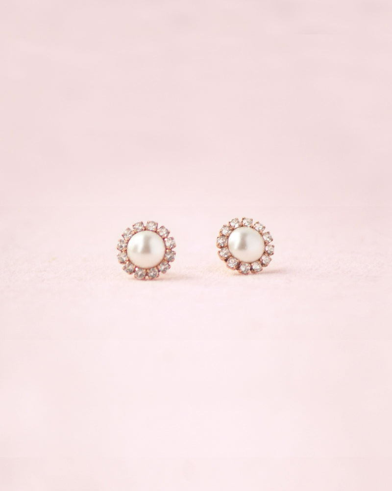 Flatlay on pink background of the Halo Pearl Stud Bridal Earrings in rose gold with cream pearls.