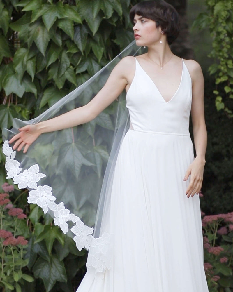 A dramatic floral lace veil is captured mid-air as a bride moves gracefully.