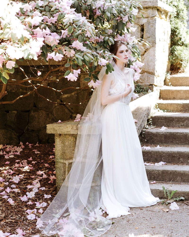 A bride wears a long single layer veil with a delicate ribbon edge.