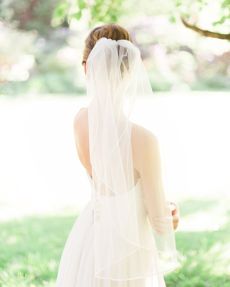 Bride wearing a short veil with delicate satin ribbon edge.