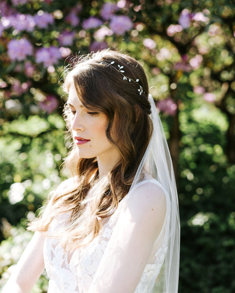 A close model view of a bride wearing the Lily Waltz Veil with a crystal hair vine in her hair.