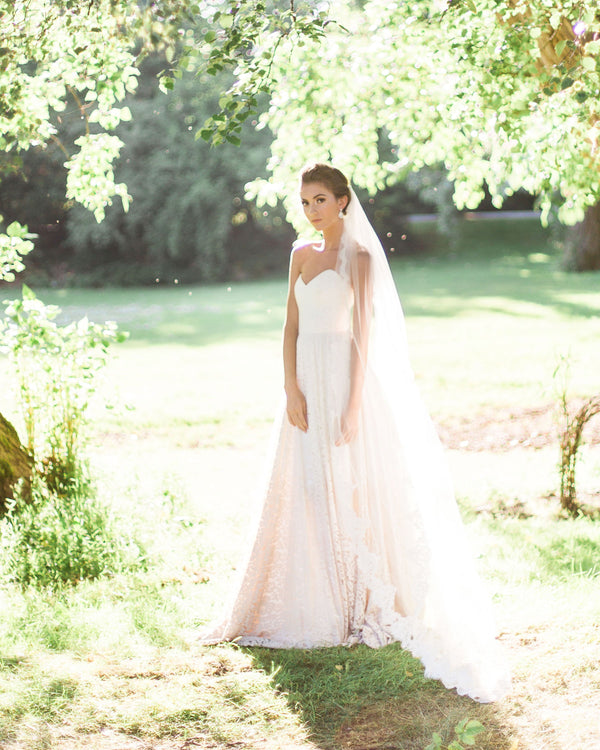 A bride is surrounded by sunlight and wears a chapel length veil with an Alencon lace edge.