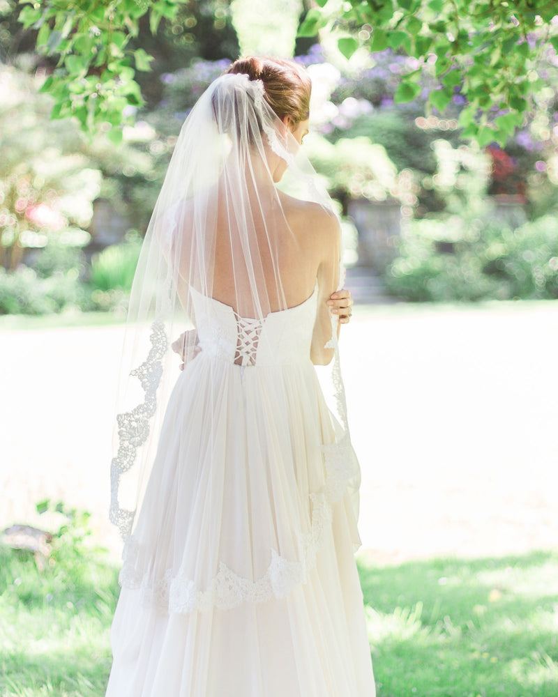 A back view of a model wearing the Magnolia Lace Veil in fingertip length with her low bridal updo.