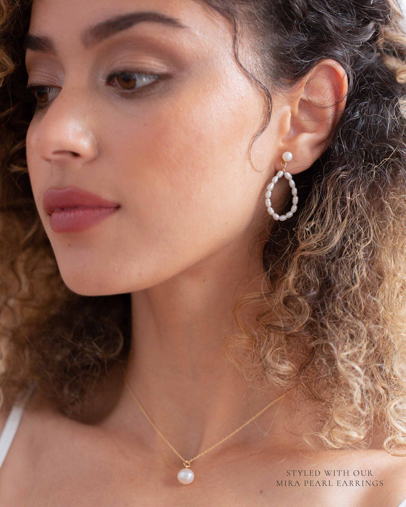 A model wears the Moondrop Pearl Necklace, paired with the Mira Pearl Earrings in gold.