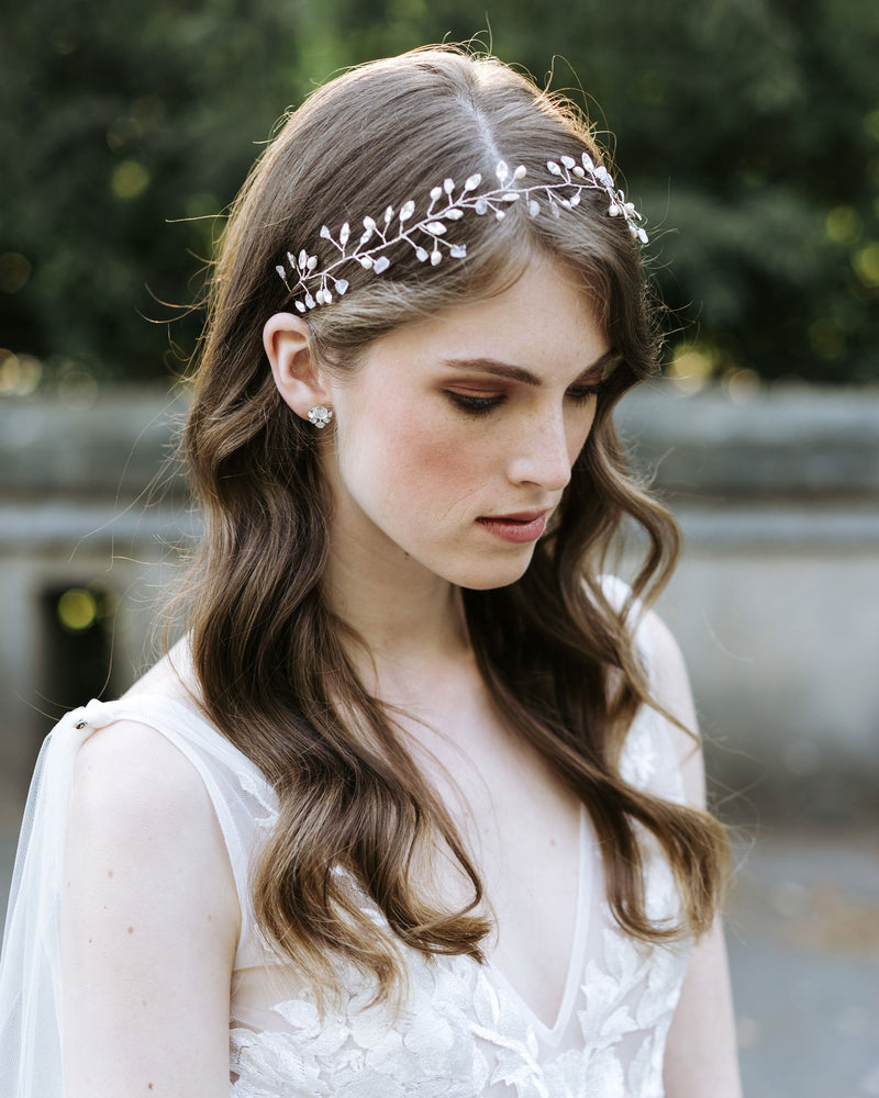 A bride wears a hair vine of scattered crystals, freshwater pearls, and moonstone. Her hair is styled in soft bridal waves.
