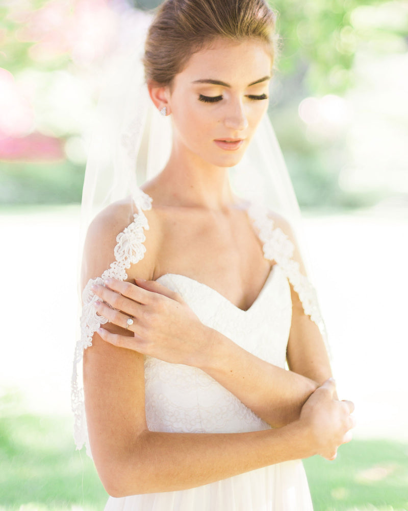 A bride wears a waist length veil with a floral lace edge.
