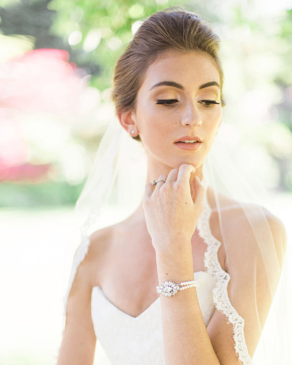 A bride wears a pearl bridal bracelet with a crystal brooch centre.