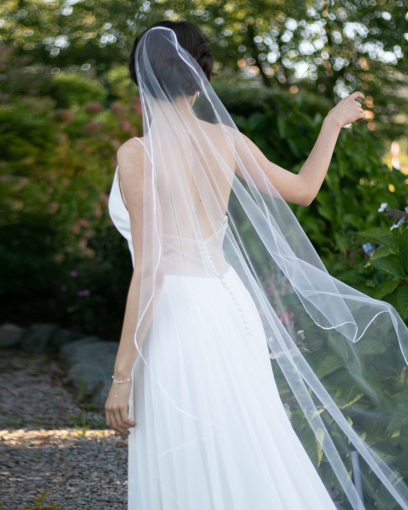 A bride wears the Primrose Ribbon Veil in cathedral length in light ivory.