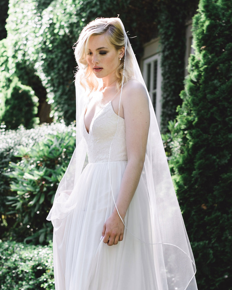 A bride wears the Primrose Veil; a waltz length veil with ribbon edge and no gathers.